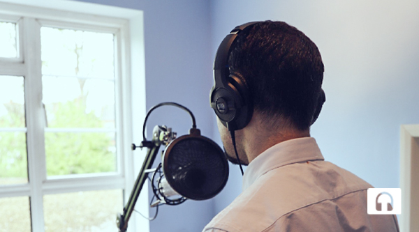 Ein Mann mit dunklen Haaren von hinten und vor ihm ein klassische Mirkofon wie aus einem Aufnahme-Studio