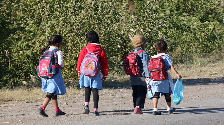 Vier junge Kinder laufen mit ihren Schultaschen auf dem Rücken eine Straße entlang
