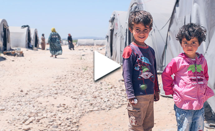 Zwei Kinder stehen vor Zelten in einem Flüchtlingslager