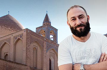 Junger Mann mit dunklem Bart und weißem T-Shirt vor einer Kirche