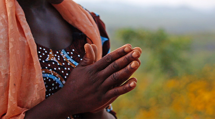 Eine afrikanische Frau faltet ihre Hände zum Gebet vor einer grünen Landschaft