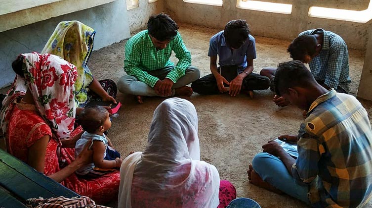 Indische Menschen sitzen im Kreis auf dem Boden und haben ihre Köpfe geneigt