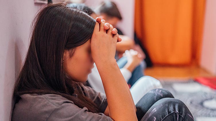 Seitenprofil eines Mädchens mit dunkelbraunen Haaren das ihr Gesicht mit gefalteten Händen bedeckt