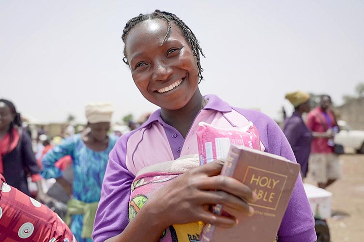 Nigerianische Frau mit violetten Klamotten mit Bibel in der Hand