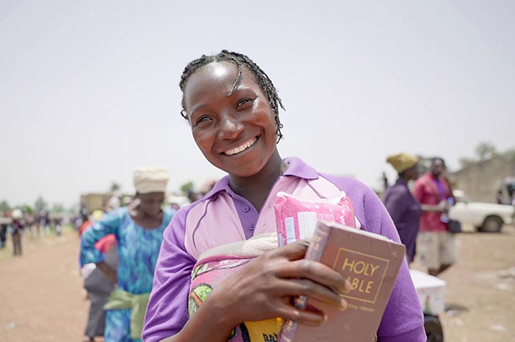 Eine verfolgte Christin hält freudestrahlend ihre Hilfsgüter und ihre Bibel in Händen.