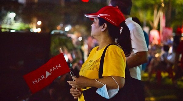 Eine Frau mit einer roten Flagge steht draußen im Dunkeln mit mehreren Menschen im Hintergrund