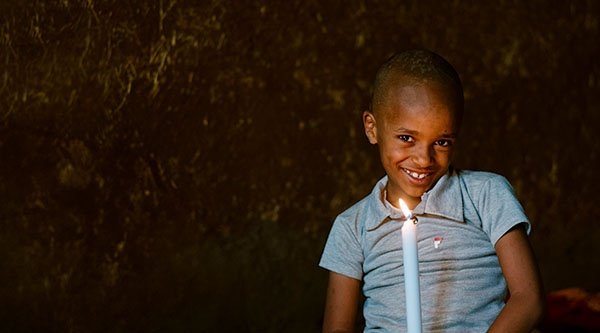 Ein kleiner Junge mit einer Kerze in den Händen grinst