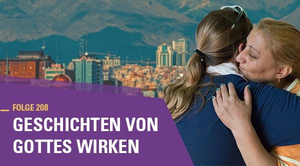 Zwei Frauen umarmen sich. Im Hintergrund ist eine Stadt vor einer Berglandschaft.