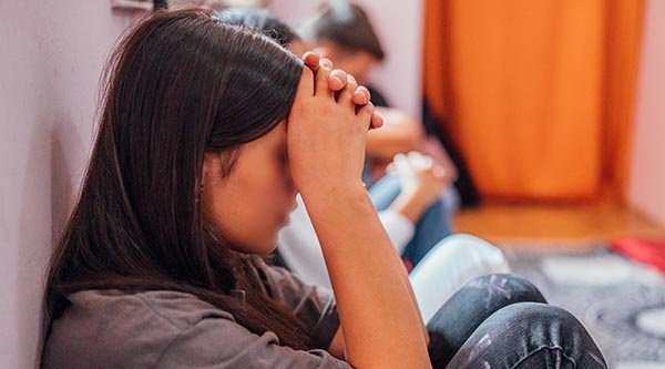 Seitenprofil eines Mädchens mit dunkelbraunen Haaren das ihr Gesicht mit gefalteten Händen bedeckt