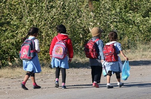 Vier junge Kinder laufen mit ihren Schultaschen auf dem Rücken eine Straße entlang